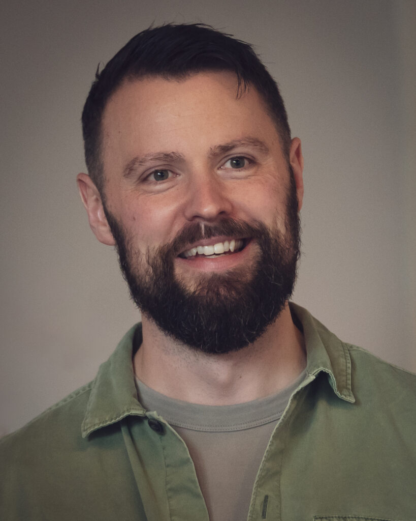 A smiling white man with short brown hair and a brown beard, wearing a khaki shirt.